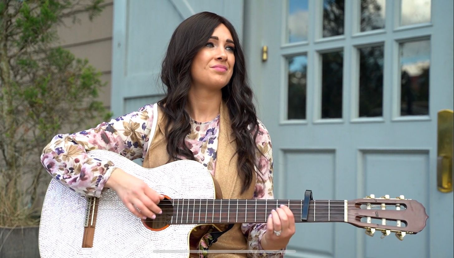 Shaindel Antelis in a floral blouse holding her rhinestone guitar